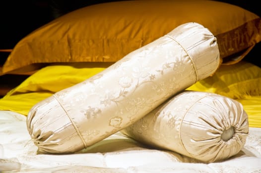 two silk cylindrical pilows on a bed 