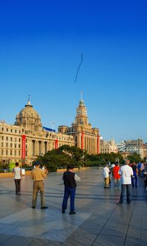 old people flying a kite on the shanghai bund at sunrise