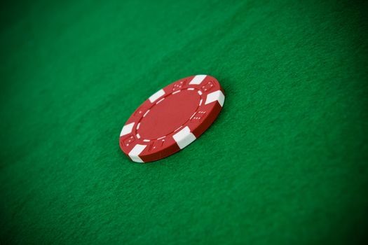 Single red poker chip on green poker table.
