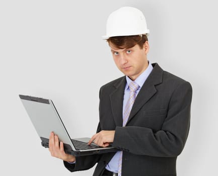 The construction superintendent with the computer in hands in a helmet on a grey background