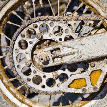 The rear wheel of a motorcycle with a chain, covered with dirt