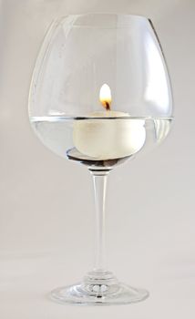 A lighted floating candle in the water in a big glass