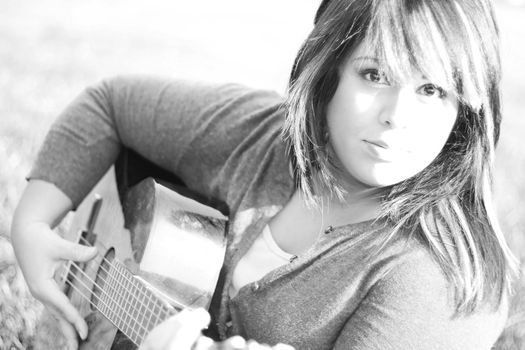 A young hispanic woman playing a guitar outdoors in black and white.