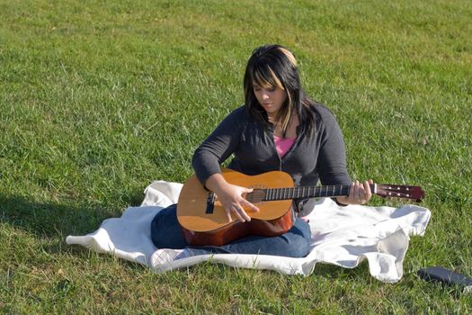 A young hispanic woman playing a guitar outdoors.