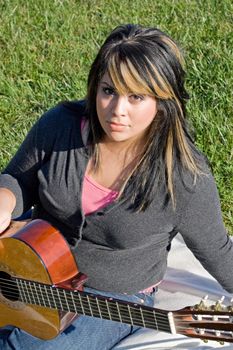 A young hispanic woman playing a guitar outdoors.