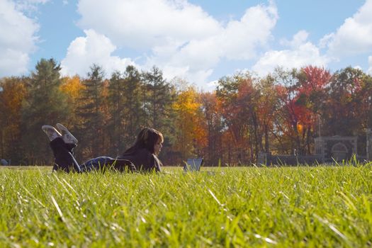 A young student using her laptop computer while laying in the grass on a nice day.