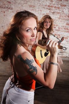 Woman sings along with guitar in front of a brick background