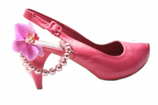 A pink high heel ladies shoe, a pearl necklace and an orchid