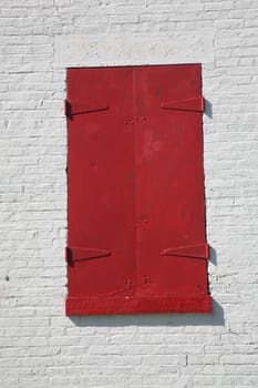Bright red lighthouse window, closed and latched, against a white brick wall