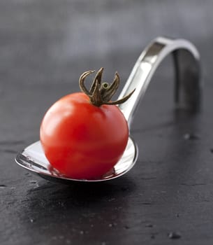 Little red tomato over an elegant restaurant metal spoon