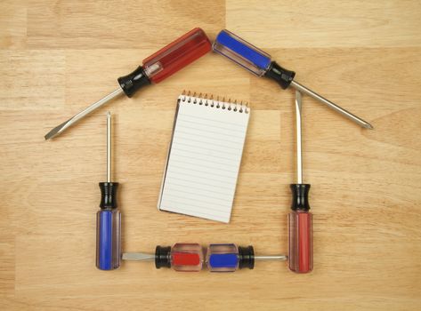 House Shaped by Screwdrivers and Pad of Paper on a Wood Background.