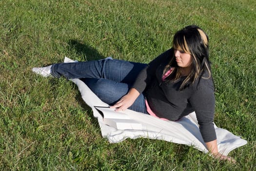 A young woman with highlighted hair reading a book on the school campus.