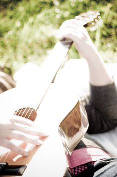 A young woman playing a guitar outdoors.