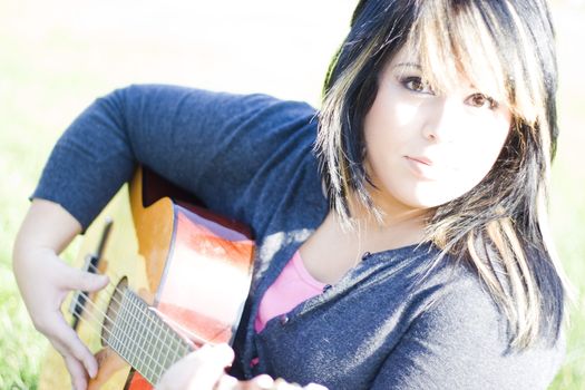 A young hispanic woman playing a guitar outdoors.