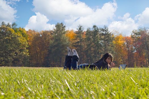 A young student using her laptop computer while laying in the grass on a nice day.