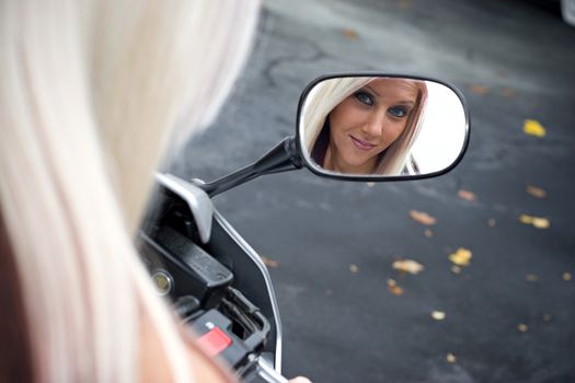 A pretty blonde woman looking into the mirror on her motorcycle.