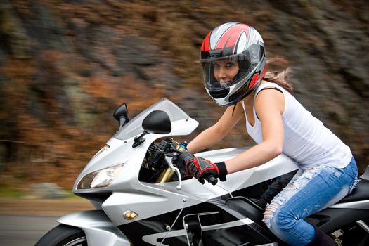 A pretty blonde girl in action driving a motorcycle at highway speeds.