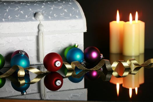 Christmas ornaments and lit candles reflecting off surface, focus on red ball and ribbon