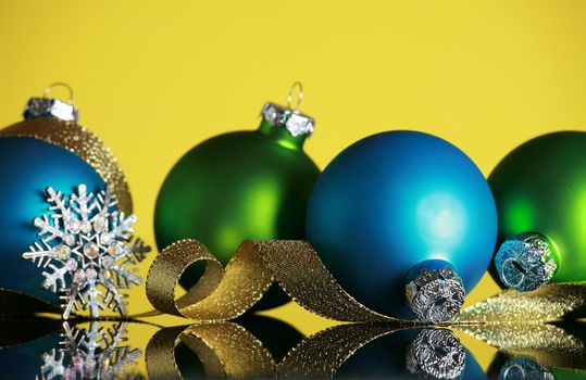 Christmas ornaments and snowflake on yellow background, focus on blue ball and gold ribbon