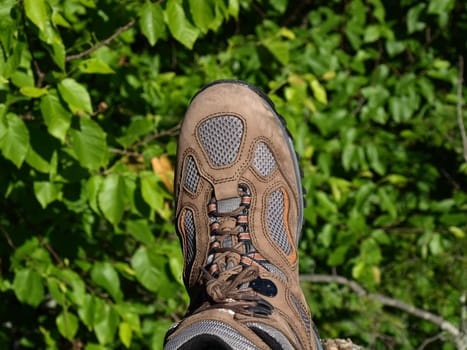 One foot hanging on the edge of mountain side.  A brown hiking boot.