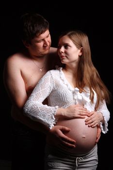 Expecting parents looking at each other and man embracing belly of his wife 