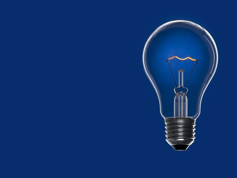 A light bulb over a blue background. Tungsten glowing filament. Copy space.