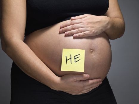 Pregnant woman with a sticky note saying HE on her belly.