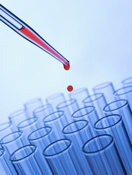 Close up of a pipette dropping a red sample into a test tube.