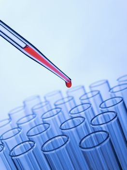 Close up of a pipette dropping a red sample into a test tube.