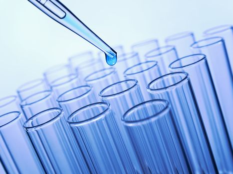 Close up of a pipette dropping a blue sample into a test tube.