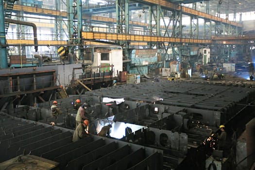 Welders welding a metal part in a dark industrial environment.