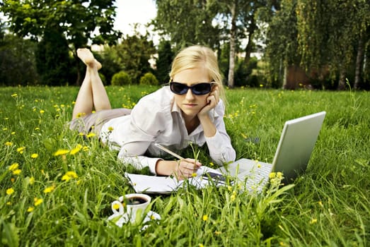 young woman working outside on computer and drinking coffee