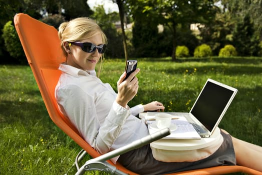 young woman working outside on computer and drinking coffee