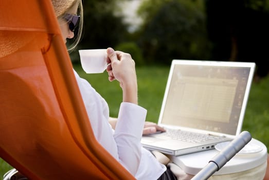 young woman working outside on computer and drinking coffee