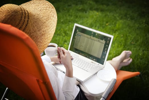 young woman working outside on computer and drinking coffee