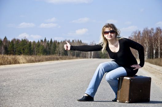 Beautiful country girl hitchhiking on the road with her baggage