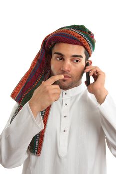 Pondering arab ethnic middle eastern businessman dressed in traditional clothing.   He is using a mobile cellphone. White background.