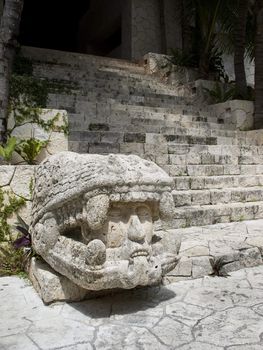 giant mayan head sculpted in stone at the bottom of the step of a mayan temple