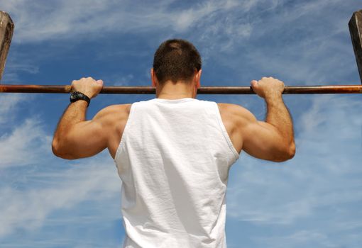 Reaching Goal: Strong Man Doing Pull-ups on a Bar in a Park