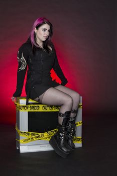 teenage girl wearing goth inspired clothes with pink and black hair sitting on a tv with a gross out expression