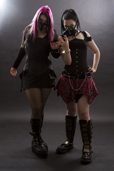 teenage girls wearing goth inspired clothes with pink, black hair and gas mask, shackle together by handcuffs