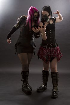 teenage girls wearing goth inspired clothes with pink, black hair and gas mask, shackle together by handcuffs