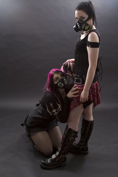 crazy looking teenage girls wearing goth inspired clothes with pink, black hair and gas mask, as the mistress pulls on the hair of the slave
