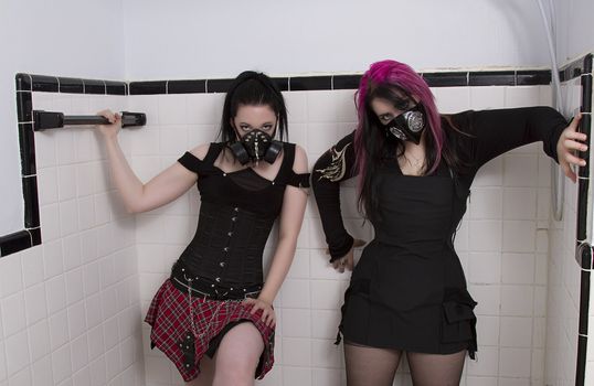crazy looking teenage girls wearing goth inspired clothes with pink and black hair wearing novelty gas mask standing in a shower