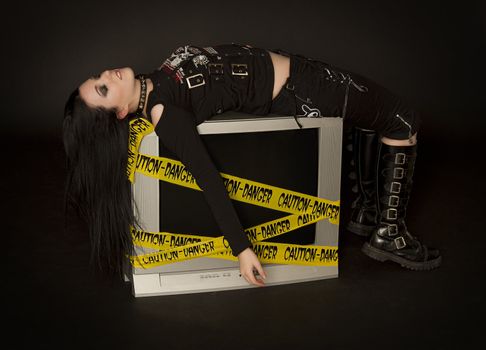 Teenage girl in goth style clothes laying on a television 