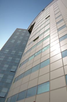 Office building with a hinged facade. Part of the facade opaque aluminum panel, part of - a complete glazing. Against the background of blue sky. Vertical orientation.