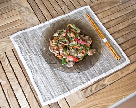 Plate with grilled vegetables and chopsticks. On wooden table.