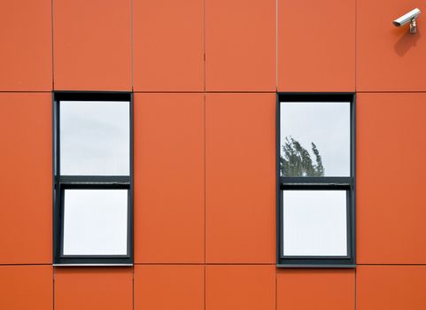 Orange facade of aluminum panels. Two windows and surveillance cameras, which looks onto the street. Close-up. Fragment.