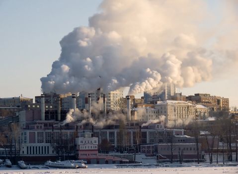 Winter urban landscape. From pipe factory fells smoke into the blue sky.