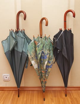 Three closed umbrellas standing at wall on package to floor